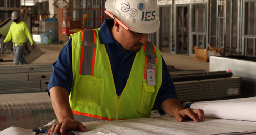 a supervisor in an Ĵý hard hat inspecting blueprints on a construction site
